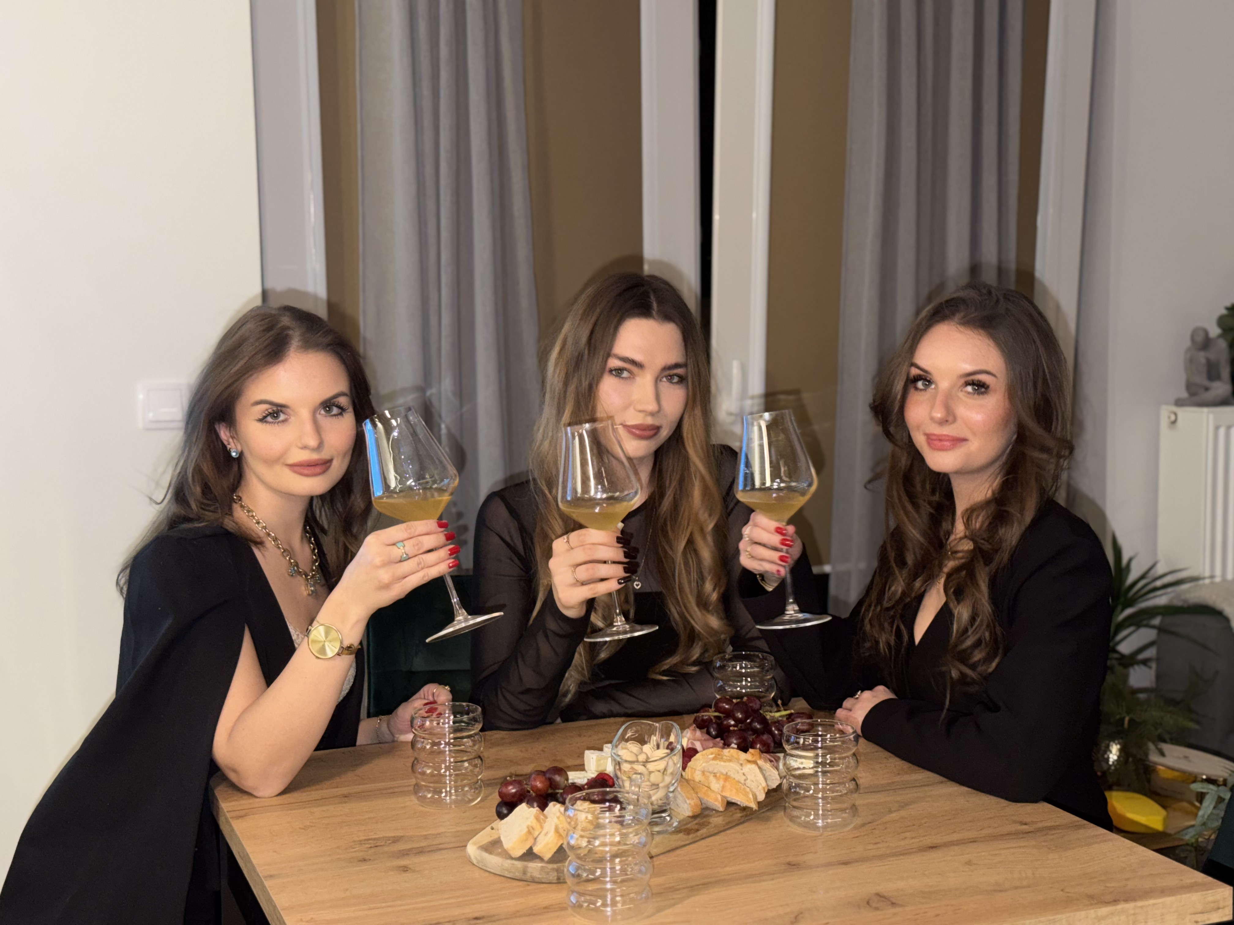 Trzy elegancko ubrane kobiety wznoszą toast kieliszkami z białym winem podczas degustacji na wieczór panieński organizowanej przez Ta od Wina